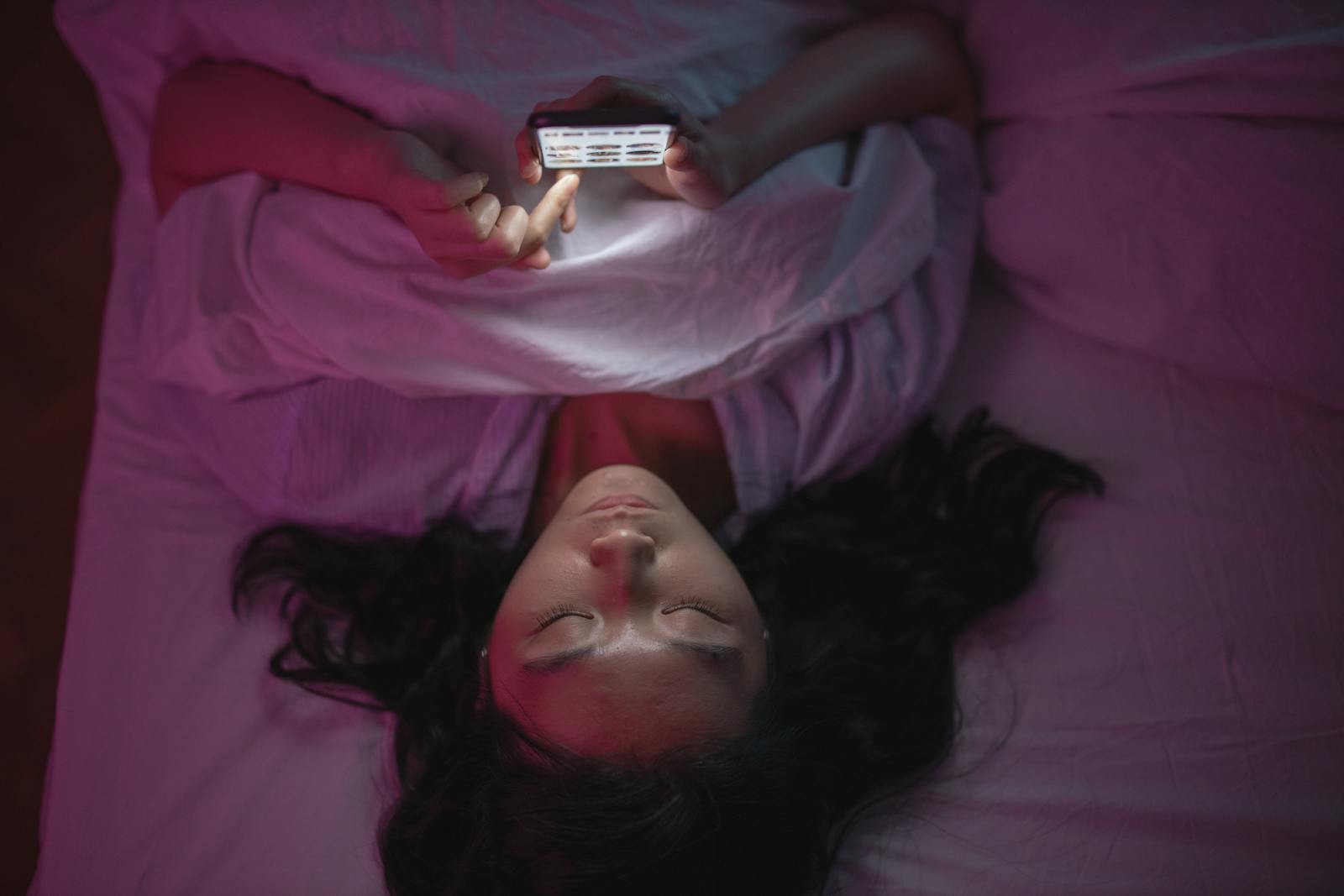 Photo by cottonbro studio A woman lying in bed at night browsing her smartphone under soft lighting.