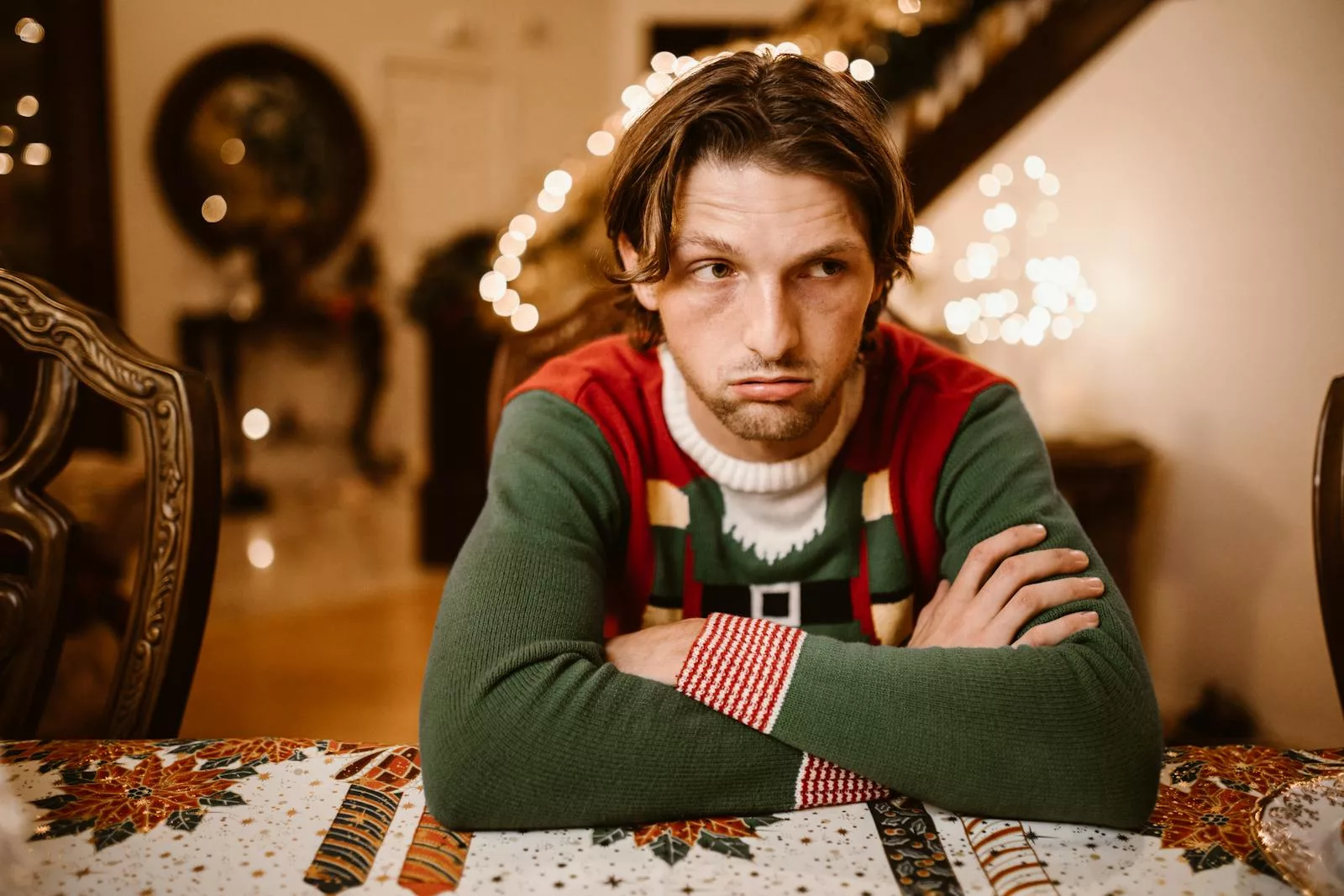 A man wearing a festive Christmas sweater looking thoughtful and contemplative indoors.